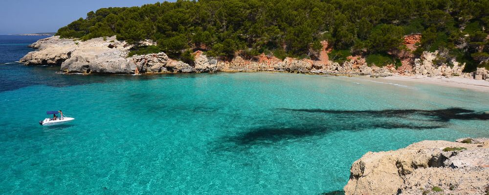 Piccola barca sul mare turchese della bellissima spiaggia di Cala Escorxada