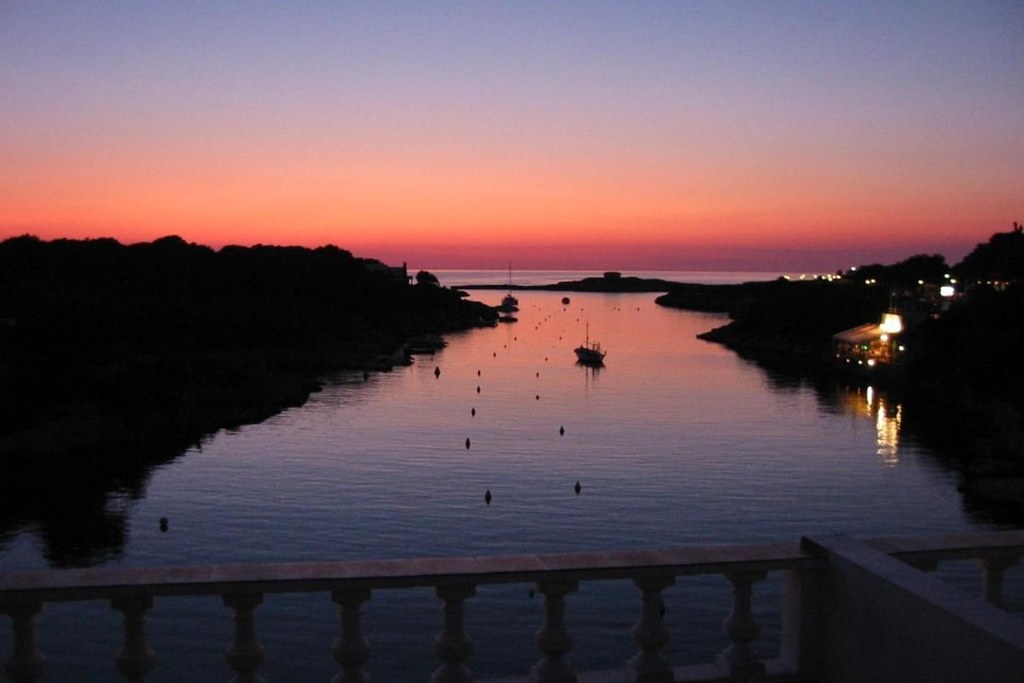Tramonto sulla cala di Cala Santandria, a Minorca, con una barca all'ancora